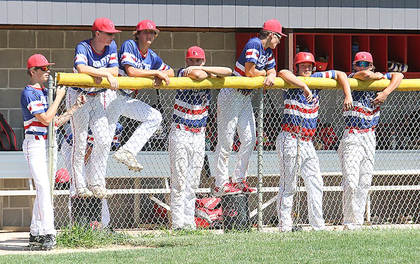 Members of the Crete Post 147 juniors team watch the game from the dugout July 6. Some used buckets to see over the yellow plastic barrier.