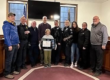 Officer Jeff Kramer's son Ryan proudly holds the Life Saving Award presented to his father. Kramer (plaid) was surrounded by his fellow officers at the council meeting on March 21.