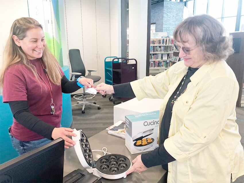 Library patron Carol Vlasin, (right), checks out the mini donut maker from librarian Zoraida Ramos