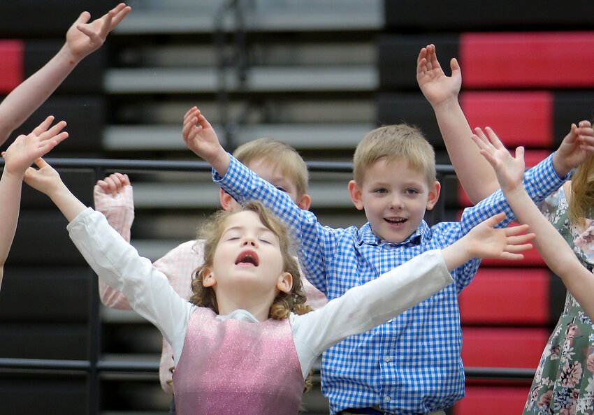 Friend kindergartneer Emerson Payne and first-graders Elijah and Kyle Nichols sing with arms raised at the Friend Spring Music Program March 19.