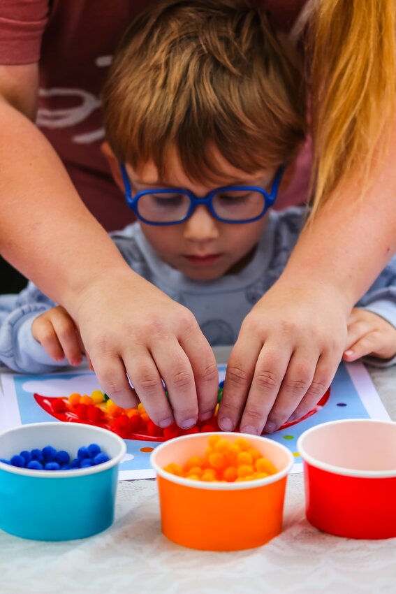 In Wilber Malcolm Nelson, 3, receives a hand - or two - from his aunt making a rainbow out of pom-poms at the Dvoracek Memorial Library's first day of their summer reading program.