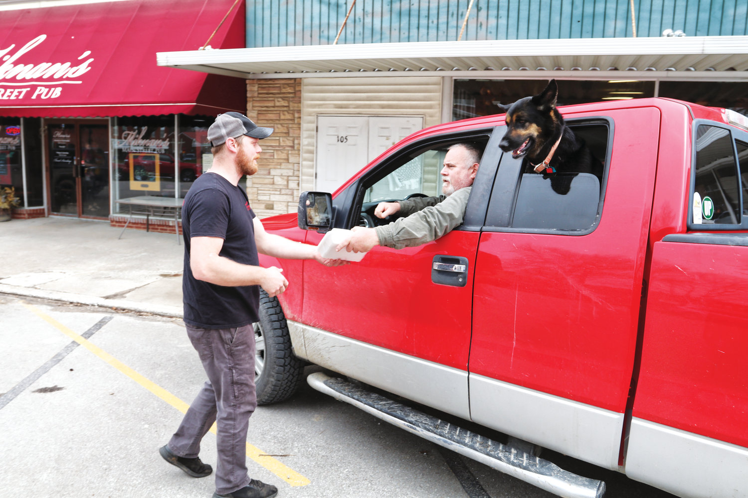 Brett Myers and his dog, Max Baer (named after the 1930s heavyweight boxing champion), enjoy curb-side delivery from Miknan’s Main Street Pub owner Leremie Shafer.
