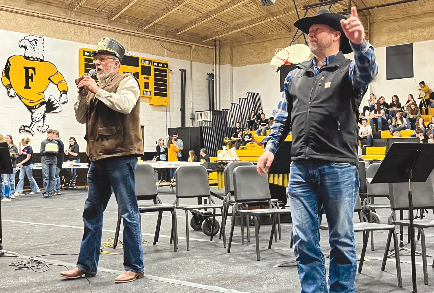 Charlie Joe (left) and Todd Flaspohler auctioned off 137 cakes, pies, and cinnamon rolls at Saturday’s annual Music Boosters Dessert Auction. When additional audience donations surpassed $500, Mr. Flaspohler (left) agreed to wear a band hat for the rest of the night.