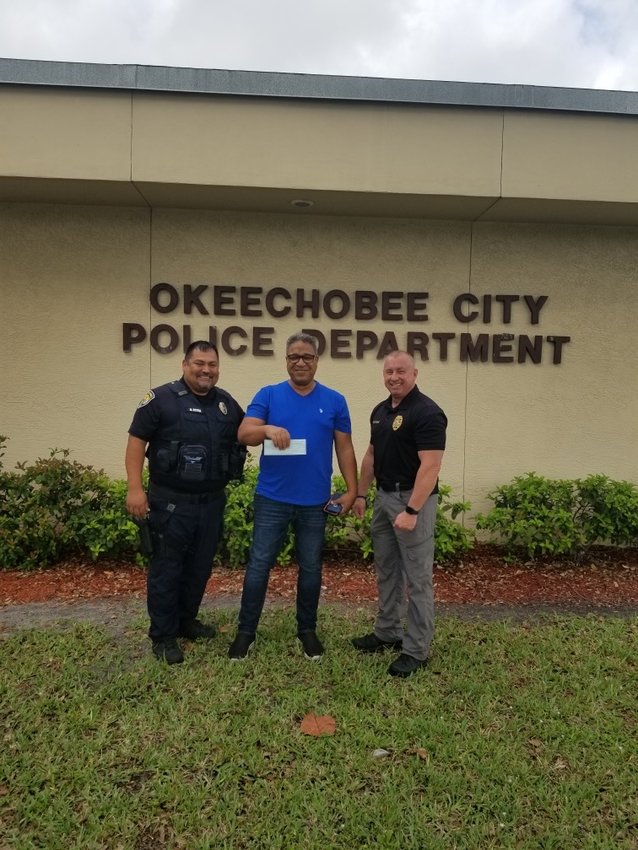 Ash Ahmed (center) presents Okeechobee City Police Chief Donald Hagan (right) and Lt. B. Reyna with a check to help pay for additional training.