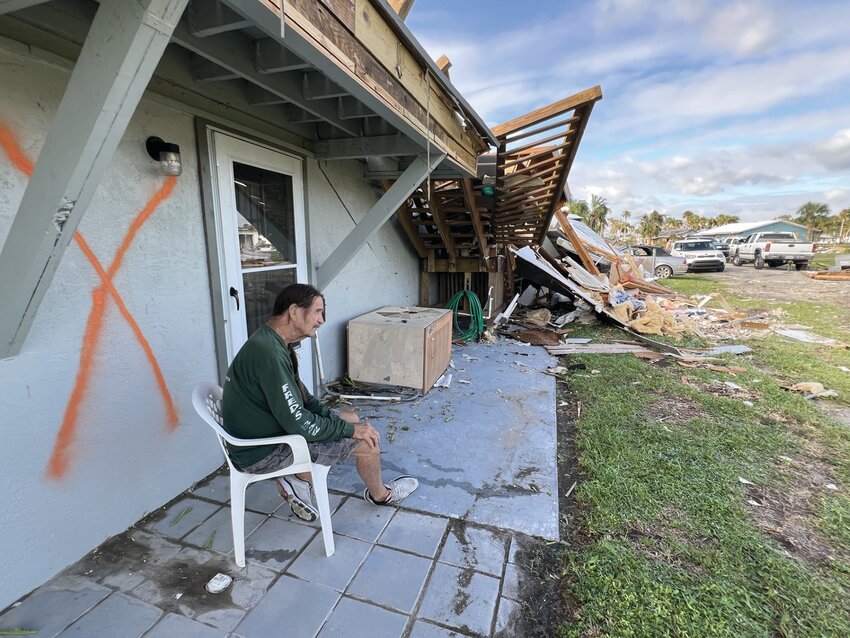 LAKEPORT -- Michael DuBose sits on the porch of his home near the Rim Canal. The 'X' on the structure indicates it was checked by search and rescue personnel after the tornadoes hit. [Photo by Katrina Elsken/Lake Okeechobee News]