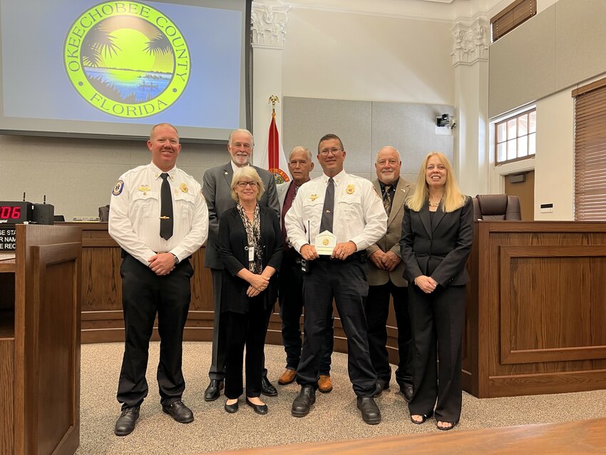 OKEECHOBEE -- Justin Hazellief was promoted to Deputy Fire Chief at the July 13 meeting of the Okeechobee County Commission. Left to right (front row) are Fire Chief Earl Wooten, Commissioner Kelly Owens, Justin Hazellief, County Administrator Deborah Manzo, (back row) Commissioner Terry Burroughs, Commission Chairman David Hazellief and Commissioner Frank DeCarlo.