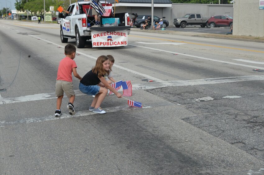 OKEECHOBEE -- Children pick up American flags tossed onto the pavement by the Republican Club's parade entry in the Speckled Perch Festival Parade. [Photo by Katrina Elsken/Lake Okeechobee News]