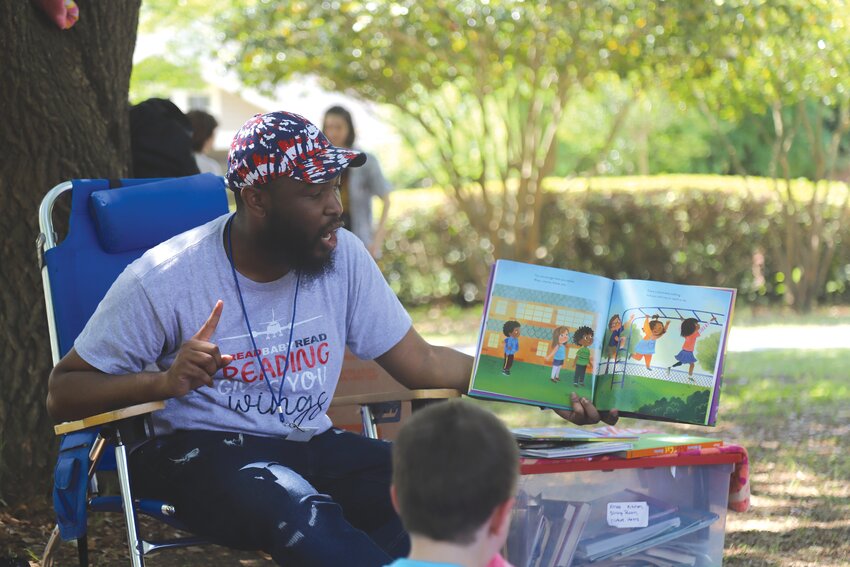 Micah Vaughn, Liberty STEAM Charter School Elementary Academy academic counselor, reads a book to children at the 16th-annual Art in the Park, hosted in Memorial Park on Saturday.