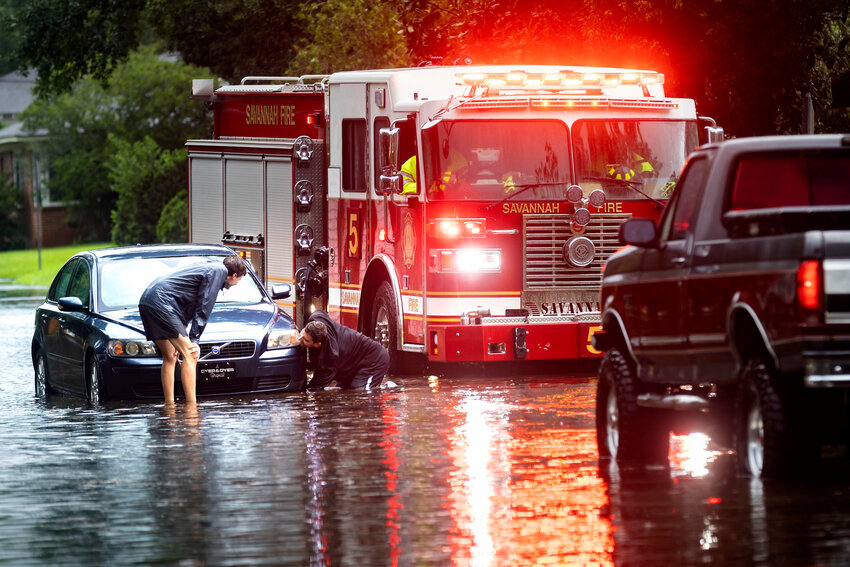 People attach a towline to a stranded vehicle on a flooded street after heavy rain from Tropical Storm Debby, Monday, Aug. 5, 2024, in Savannah, Georgia.