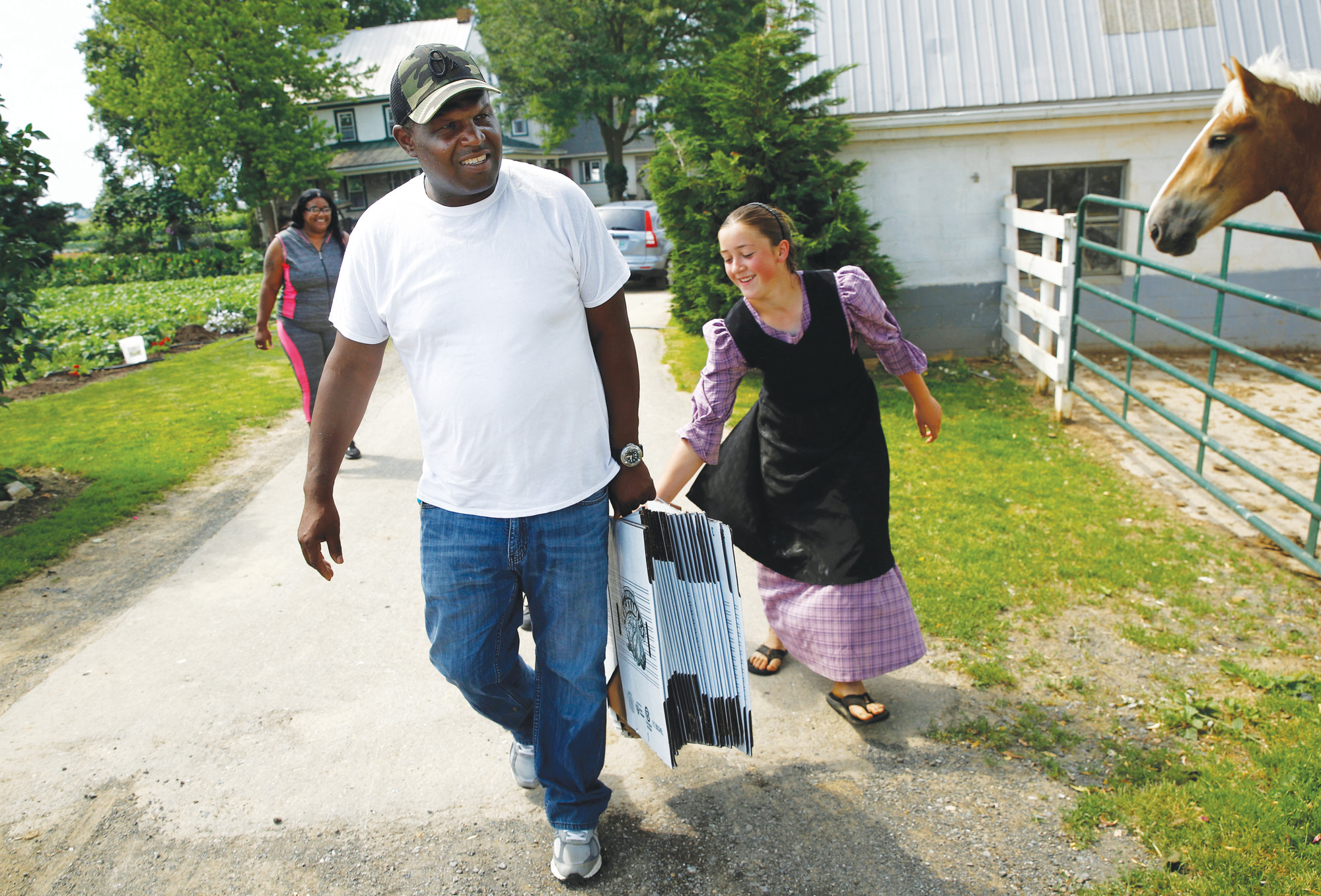 James Chase, left, the leader of a Baltimore arabber stable helps a daughter of an Old Order Mennonite family carry produce boxes at her family's farm in New Holland.