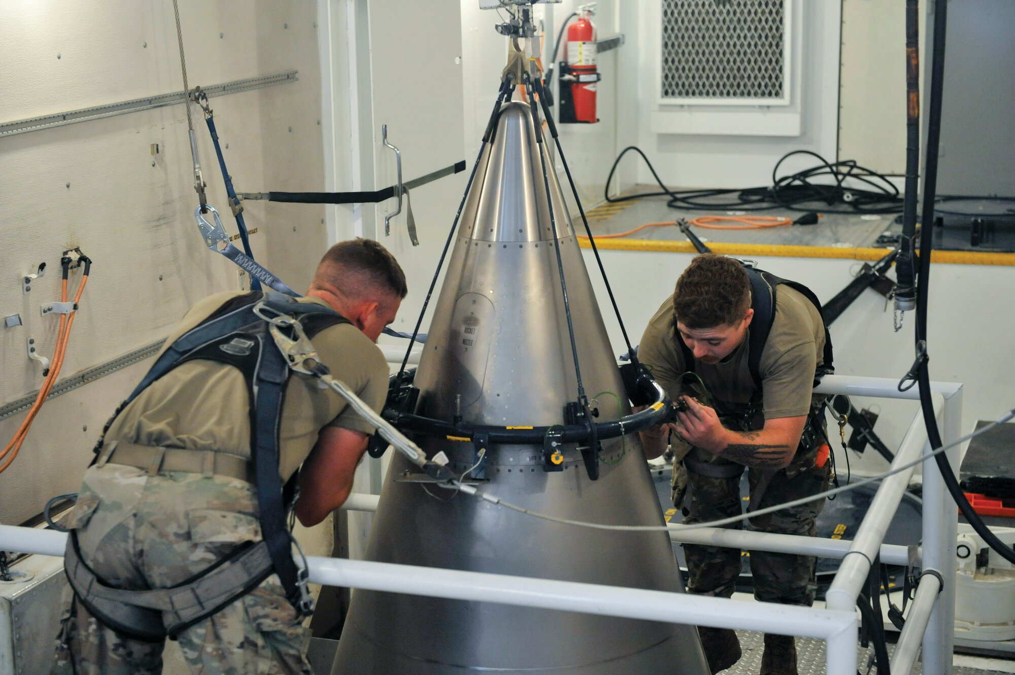 U.S. Air Force Senior Airman Jacob Deas, 23, left, and Airman 1st Class Jonathan Marrs, 21, right, secure the titanium shroud at the top of a Minuteman III intercontinental ballistic missile on Aug. 24, 2023, at the Bravo 9 silo at Malmstrom Air Force Base in Montana. After the shroud is secured, it is lifted off, revealing the black cone-shaped nuclear warhead inside.